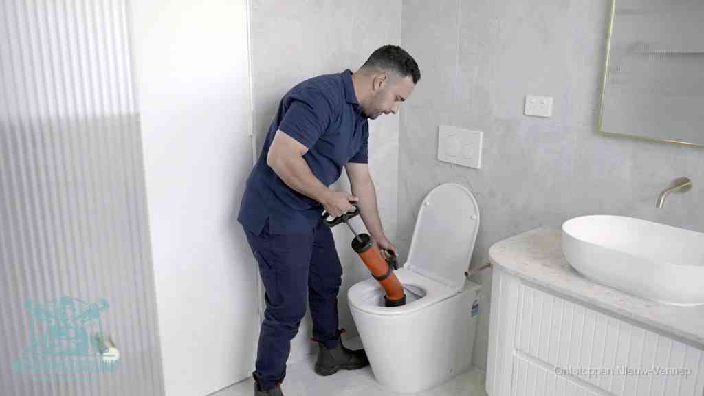 Een monteur buigt over een wandcloset en duwt met de hand een persluchtontstopper in de toiletpot om de verstopping handmatig los te maken in Nieuw-Vennep