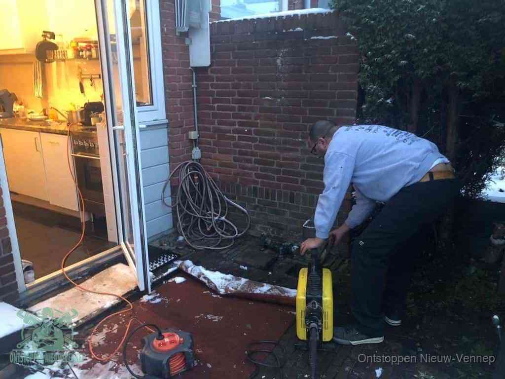 Een monteur werkt buiten bij een open riool-/grondput met een elektrische ontstoppingsmachine om een verborgen afvoerprobleem op te sporen in Nieuw-Vennep