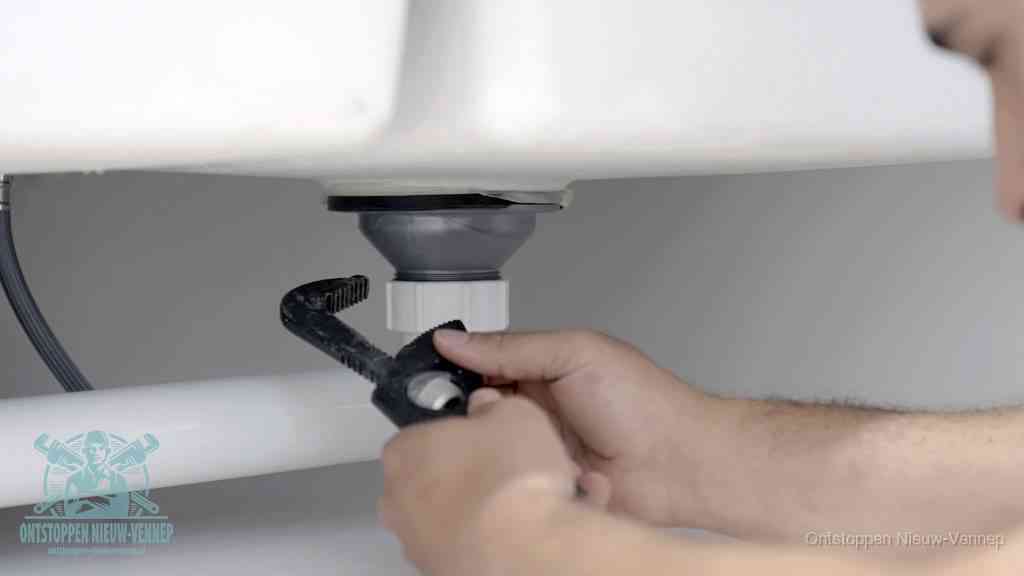 Twee handen draaien met een waterpomptang de wartelmoer van de kunststof sifon los om hem schoon te maken in Nieuw-Vennep
