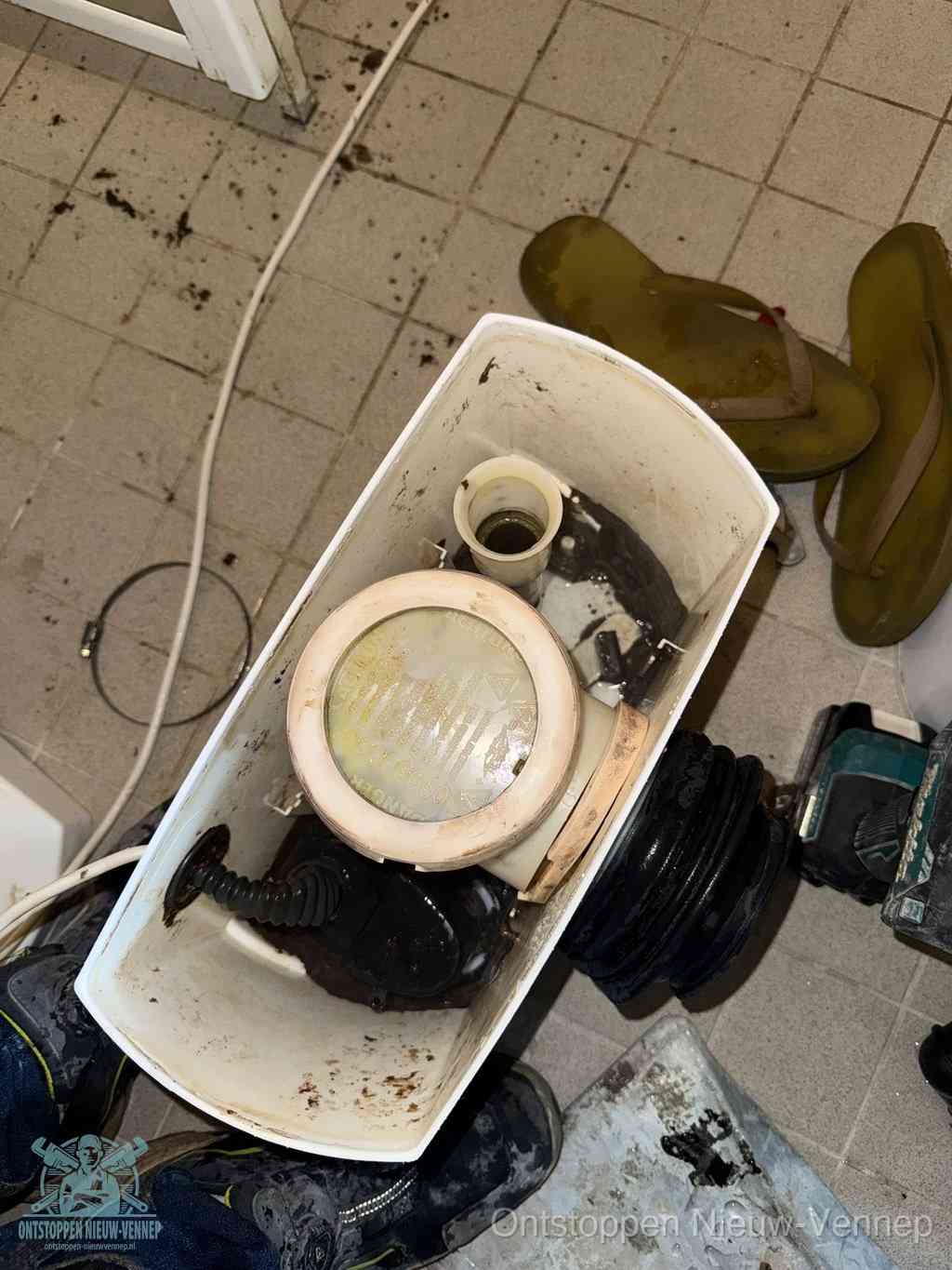 Een gedemonteerde toiletpot op de vloer met ontstoppingsveer en gereedschap ernaast, het verwijderen van een vastzittend voorwerp uit de wc in Nieuw-Vennep