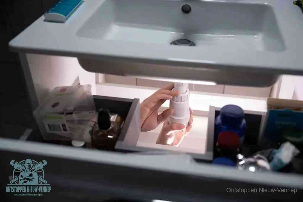 Een pompfles met zeep boven een wastafel in de toiletruimte, de warm water en afwasmiddel-methode om de wc te ontstoppen in Nieuw-Vennep
