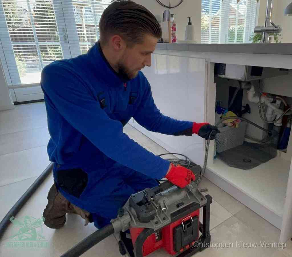 Een monteur met rode handschoenen knielt in een keuken en voert een elektrische ontstoppingsveer in tijdens het professioneel afvoer ontstoppen in Nieuw-Vennep
